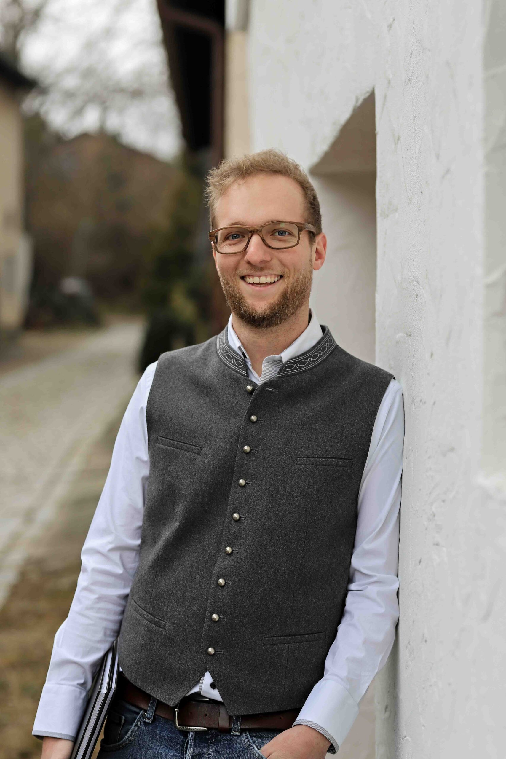 Portraitfoto von Patrick Brauchart - er lehnt an einer Wand mit Blick in Richtung Kamera - über uns